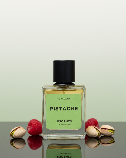 Perfume bottle labeled 'Pistache' with pistachios and raspberries on a reflective surface.